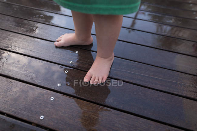 Sezione bassa della bambina in piedi nel portico bagnato a casa . — Foto stock