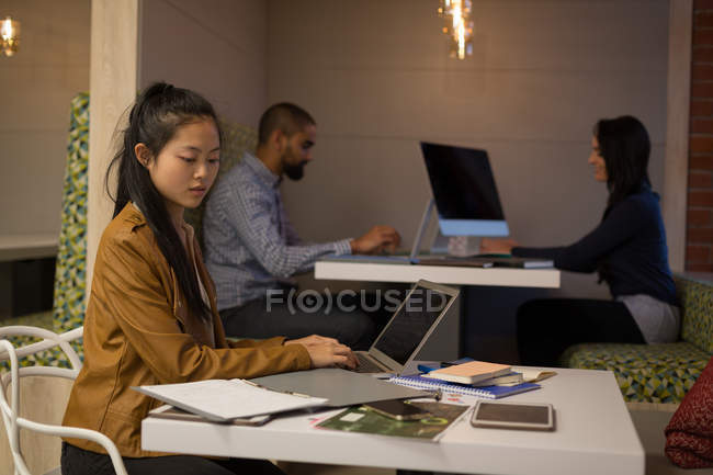 Female executive using laptop in cafeteria at office — Stock Photo