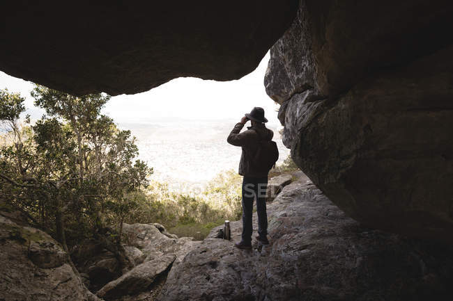 Escursionista guardando attraverso il binocolo dalla grotta — Foto stock