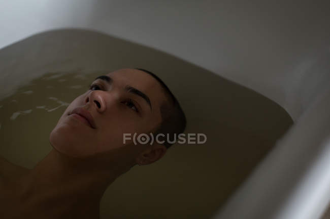 Thoughtful young man relaxing in bathtub at bathroom — Stock Photo