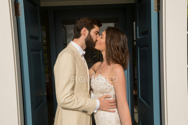 Romantic bride and groom kissing at the entrance — Stock Photo