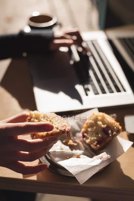 Close-up de mulher ter muffin ao usar laptop no café ao ar livre — Fotografia de Stock