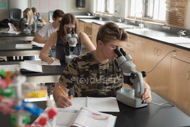 Estudiantes universitarios experimentando con microscopio en laboratorio en la universidad - foto de stock