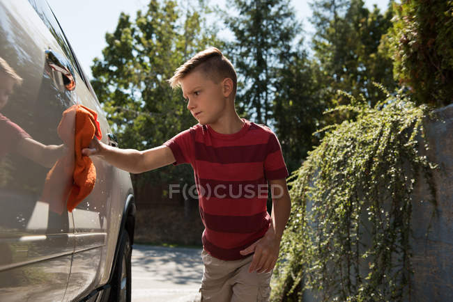 Мальчик моет машину в гараже в солнечный день — стоковое фото
