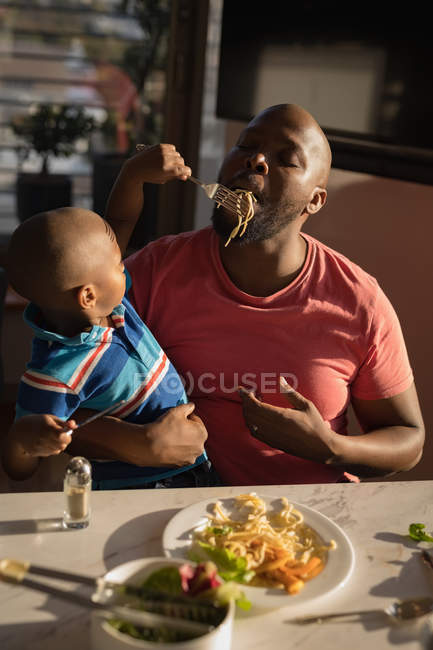 Son feeding father pasta while dinner at home. — Stock Photo
