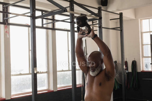 Homem sênior determinado exercitando com kettlebell no estúdio de fitness . — Fotografia de Stock
