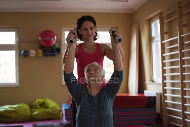 Terapeuta feminina assistindo mulher idosa com halteres em lar de idosos — Fotografia de Stock