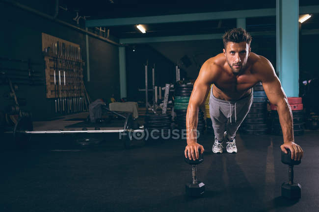 Портрет м'язистого чоловіка, який робить штовхання з гантелями у фітнес-студії — стокове фото