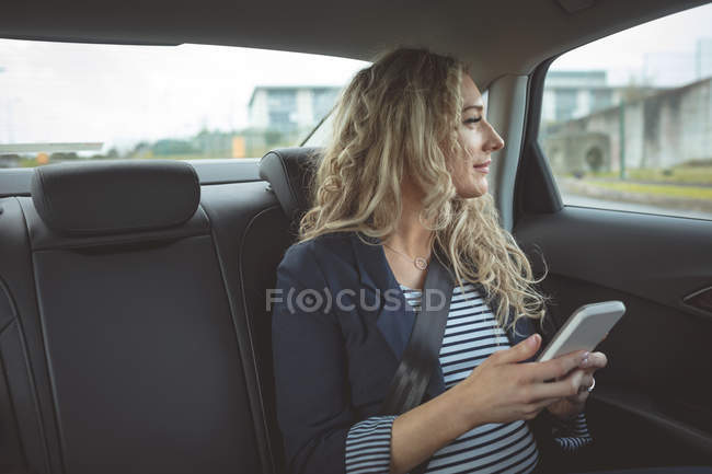 Jeune femme d'affaires utilisant un téléphone portable et regardant dehors fenêtre dans une voiture — Photo de stock
