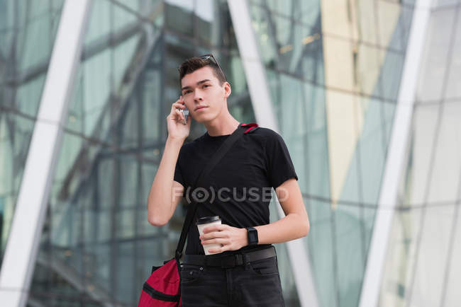Hombre hablando por teléfono móvil mientras toma café en oficinas - foto de stock