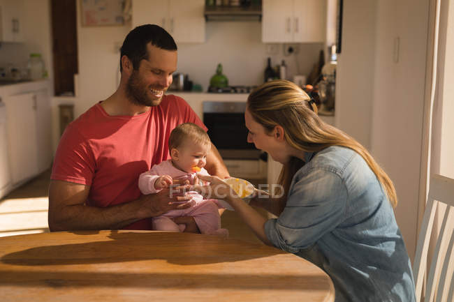 Padres felices alimentando al niño por mesa en casa . - foto de stock