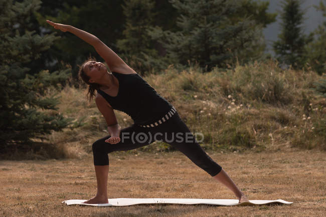 Mujer en forma realizando ejercicio de estiramiento en un terreno abierto en un día soleado - foto de stock