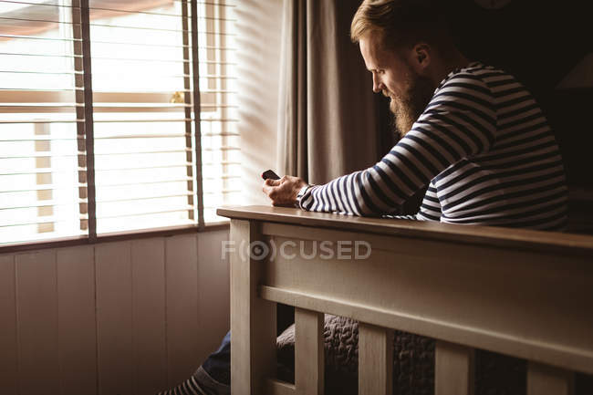 Uomo seduto sul tavolo con il cellulare a casa — Foto stock