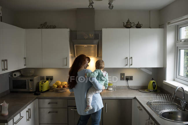 Mère tenant sa petite fille dans la cuisine à la maison — Photo de stock