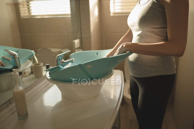 Young mom placing baby bath seat into bathroom sink at home — Stock Photo