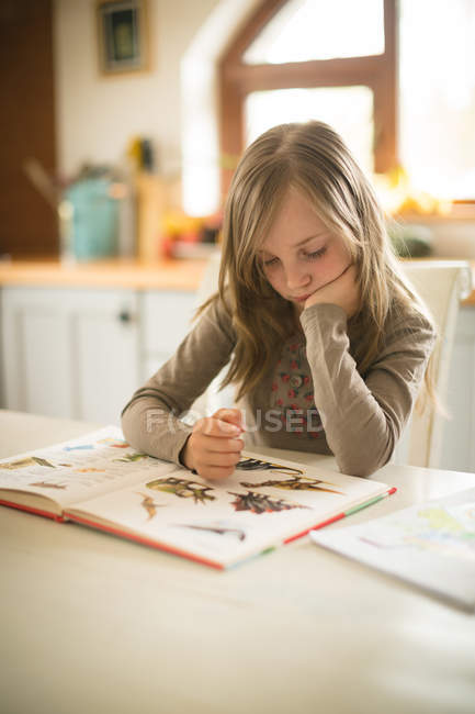 Девочка читает книгу на кухне дома — стоковое фото