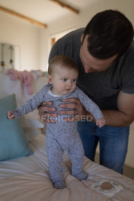 Father holding baby son on bed at home. — Stock Photo