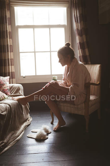 Mujer aplicando crema en el cuerpo en el dormitorio en casa . - foto de stock