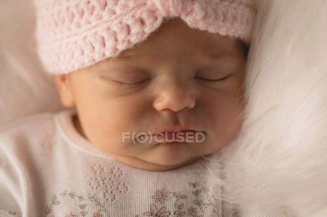 Newborn baby in knitted hat sleeping on fluffy blanket at home. — Stock Photo