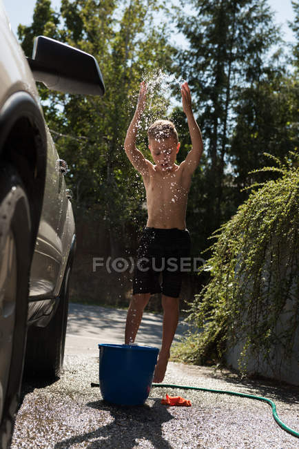 Garçon jouer avec l'eau tout en lavant la voiture au garage extérieur — Photo de stock