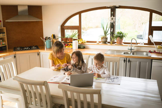 Mother helping children with homework in kitchen at home — Stock Photo