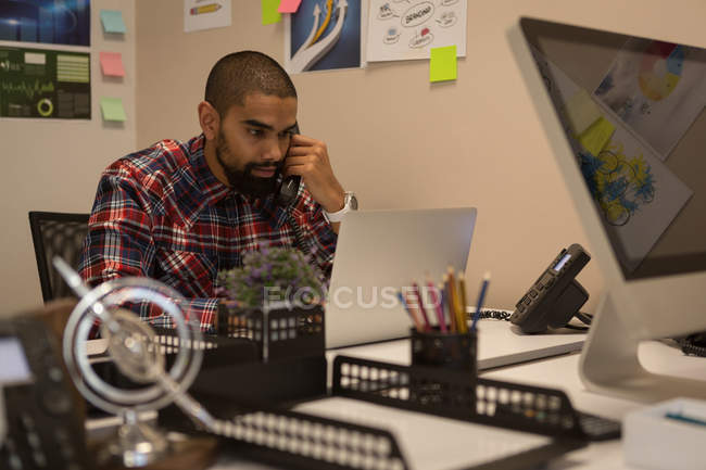 Чоловік-виконавчий розмовляє по телефону, використовуючи ноутбук в офісі — стокове фото