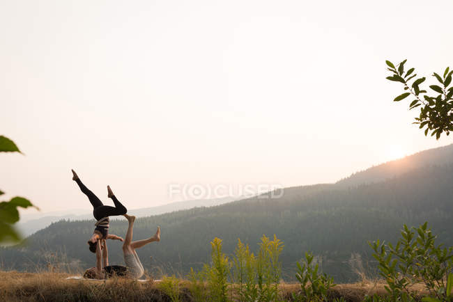 Couple sportif pratiquant l'acro yoga dans un terrain vert luxuriant au moment de dwan — Photo de stock