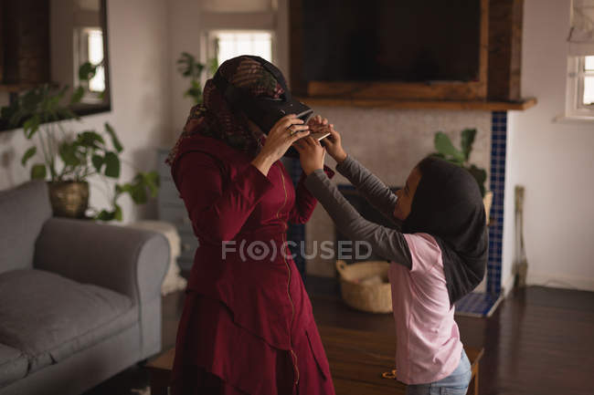 Madre e hija musulmana usando auriculares VR en casa - foto de stock