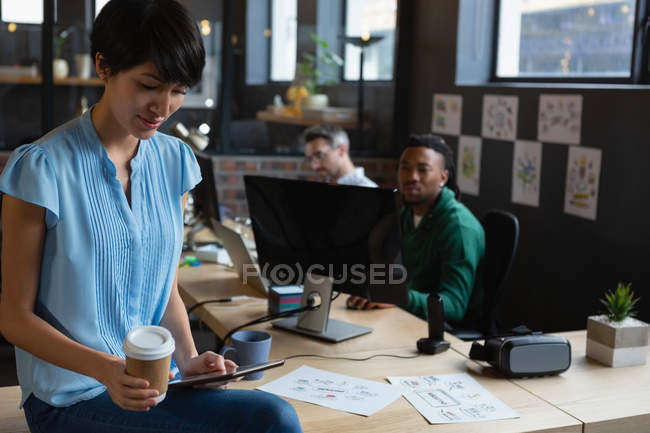 Ejecutiva femenina con café usando tableta en el escritorio en la oficina . - foto de stock
