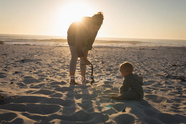 Mãe brincando com filho na praia durante o pôr do sol — Fotografia de Stock