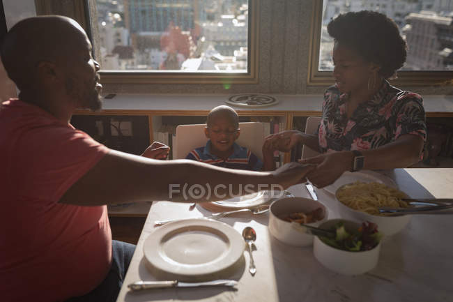 Familia con hijo rezando antes de cenar en casa . - foto de stock