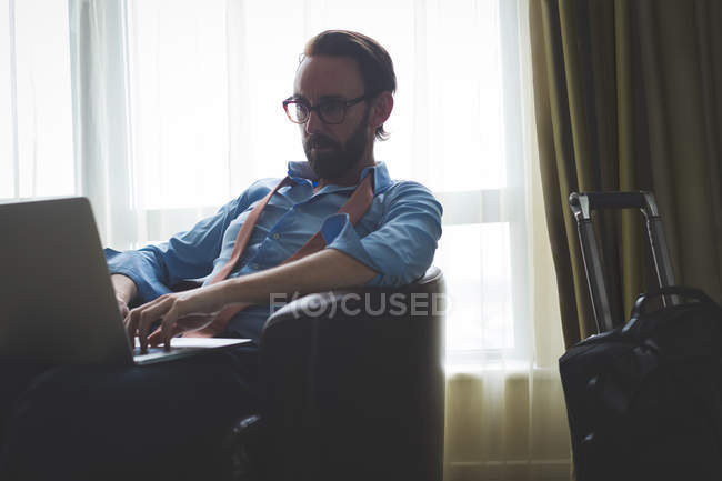 Homme d'affaires utilisant un ordinateur portable sur fauteuil dans la chambre d'hôtel — Photo de stock