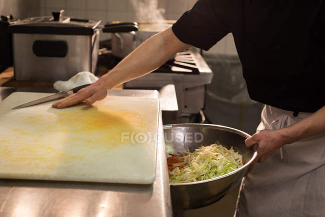 Шеф-повар кладет нарезанные овощи в большую миску на кухне — стоковое фото