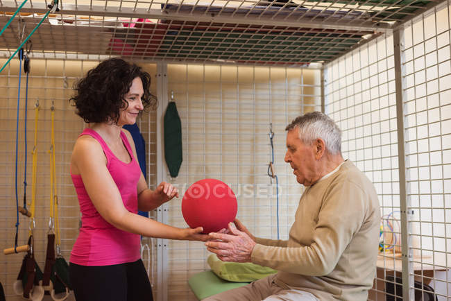 Female therapist assisting senior man with exercise ball in nursing home — Stock Photo