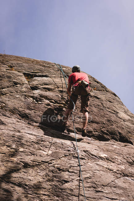Vista de ángulo bajo del escalador escalando el acantilado rocoso - foto de stock