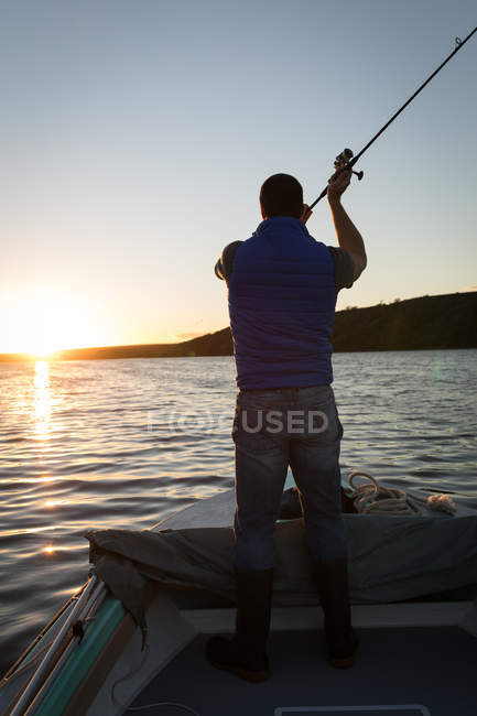 Uomo con canna da pesca in piedi in barca a motore in retroilluminazione
. — Foto stock