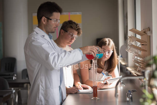 Teacher assisting students in chemical experiment at laboratory — Stock Photo
