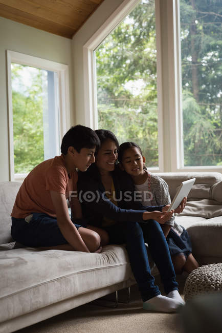 Madre e hijos que tienen videollamada en la computadora portátil en la sala de estar en casa - foto de stock