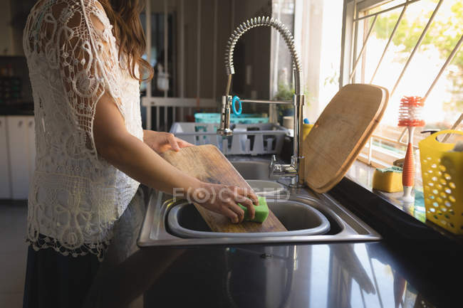 Tabla de cortar de lavado de mujer en fregadero en cocina - foto de stock