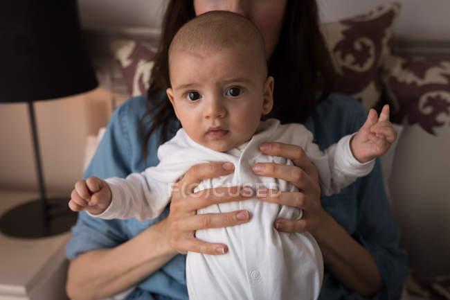 Portrait Of Cute Little Baby Looking Into Camera And Mom Holding Him