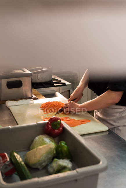 Sección media del chef picando verduras en la cocina - foto de stock