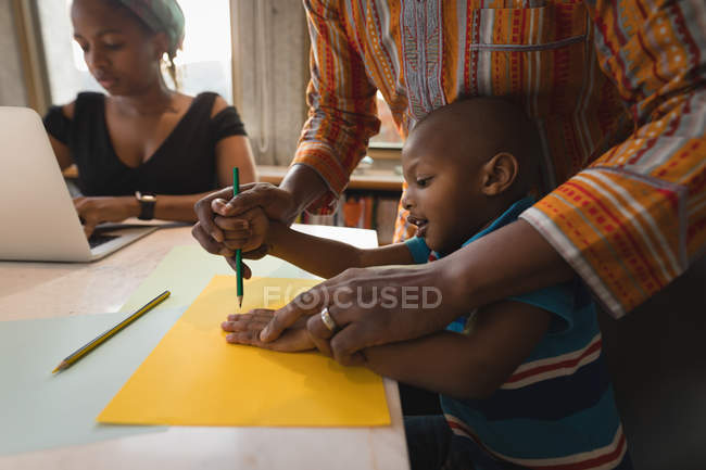 Father assisting son drawing sketch at table with woman at laptop. — Stock Photo