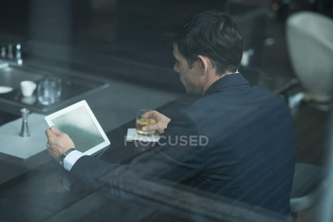 Бизнесмен, употребляющий цифровой планшет во время употребления виски на стойке регистрации отеля — стоковое фото