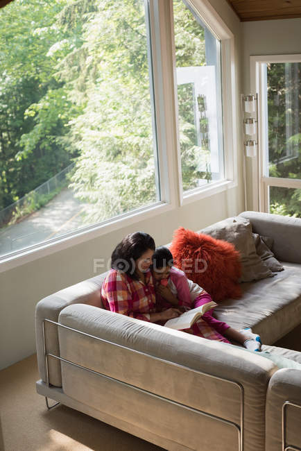 Mother and daughter reading a book in living room at home — Stock Photo