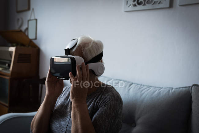 Femme âgée utilisant casque de réalité virtuelle dans le salon à la maison — Photo de stock