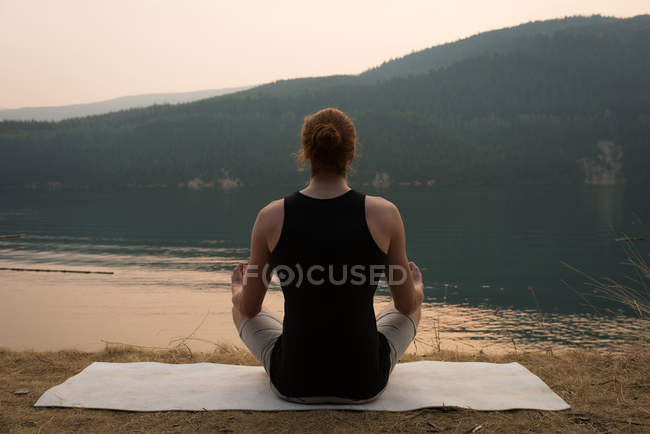 Vista posterior del hombre en forma sentado en postura de meditación en un terreno abierto - foto de stock