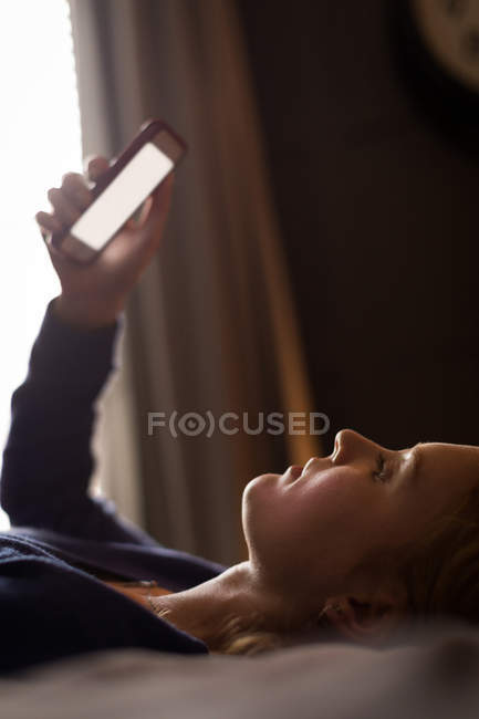 Gros plan de la jeune femme allongée sur son lit à l'aide de son téléphone portable — Photo de stock