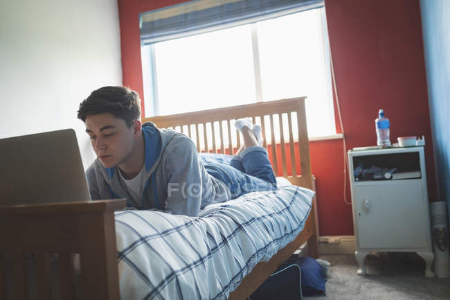 Junger Mann liegt vor und benutzt Laptop im Schlafzimmer. — Stockfoto