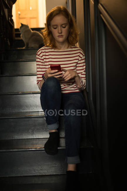 Young woman sitting on staircase using her mobile at home — Stock Photo