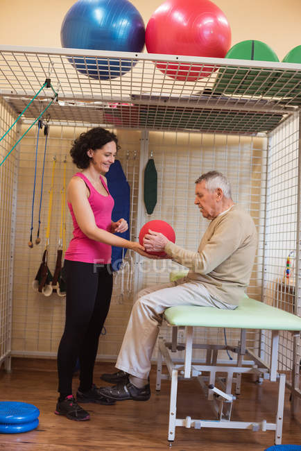 Female therapist assisting senior man with exercise ball in nursing home — Stock Photo